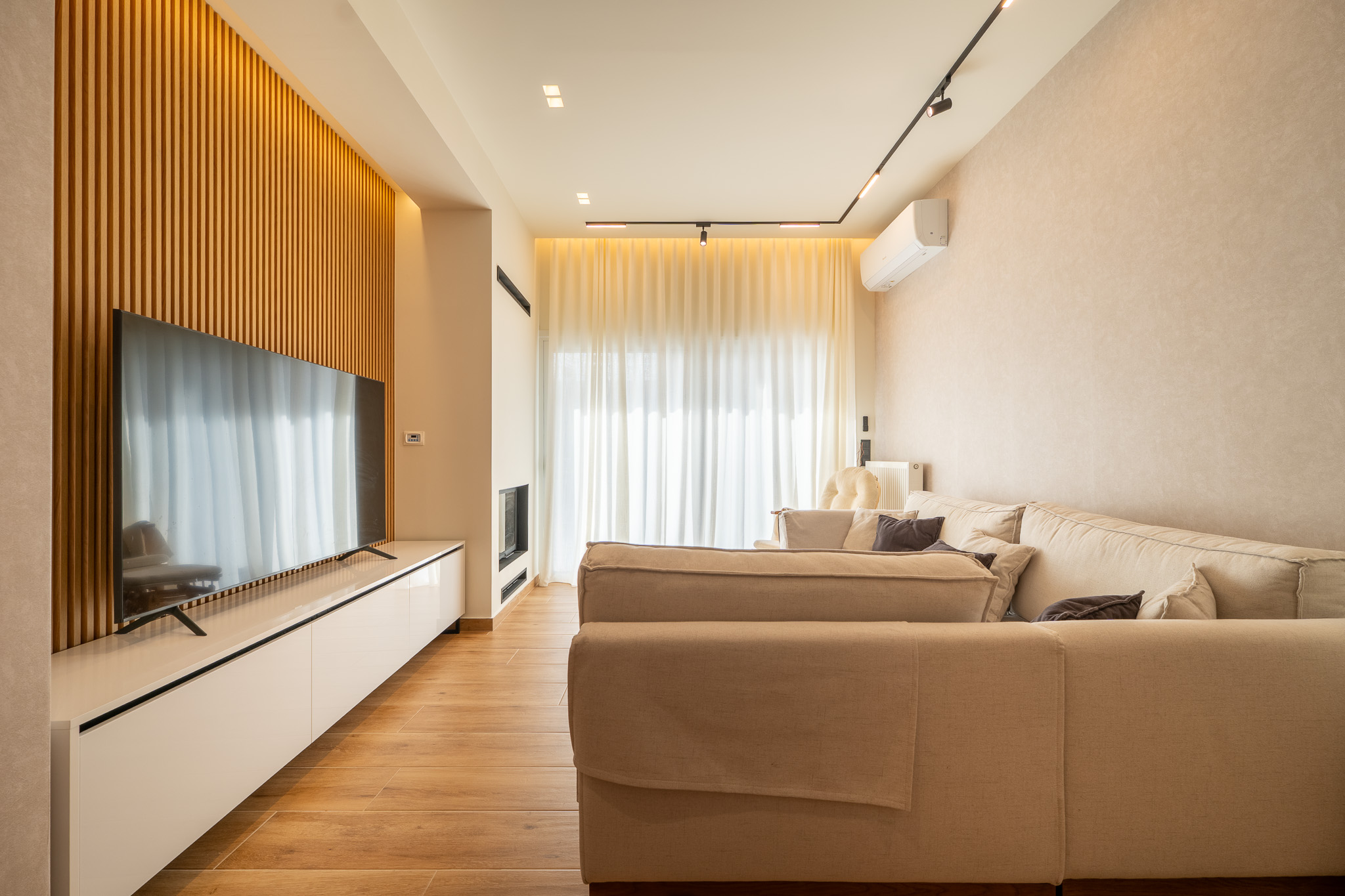 A&K Chorothetisis, beige linen sofa facing wall-mounted TV on oak slats